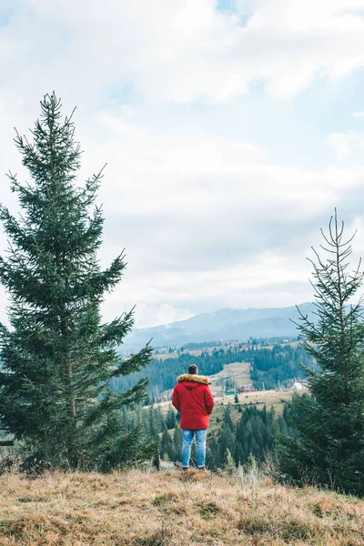 Homme en manteau rouge debout à la falaise avec belle vue sur les montagnes — Photo