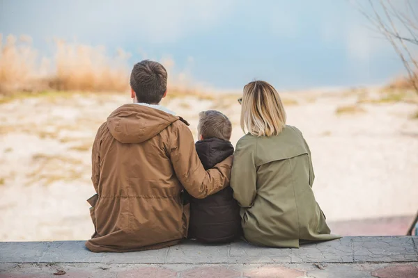 Joven hermosa familia sentada en la playa con vista al lago —  Fotos de Stock