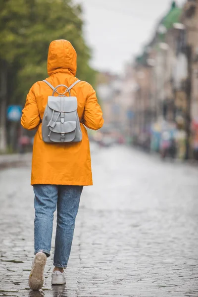Женщина в желтом плаще прогуливается по улицам города под дождем — стоковое фото