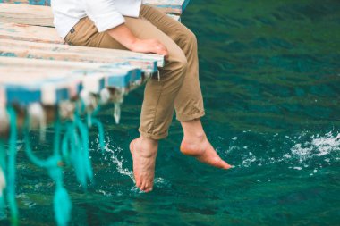 asma köprüde oturan kırpma resim adam deniz suyuna bacaklar koymak