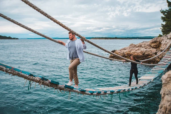 Casal mulher com homem andando por ponte de suspensão instável cruzando baía do mar — Fotografia de Stock