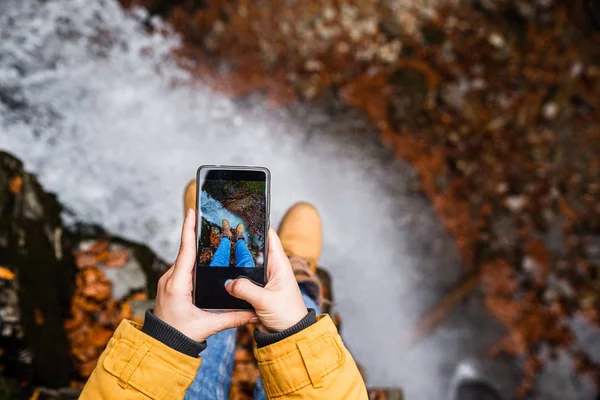 Mujer tomando la foto en el teléfono de sus piernas con cascada en el fondo — Foto de Stock