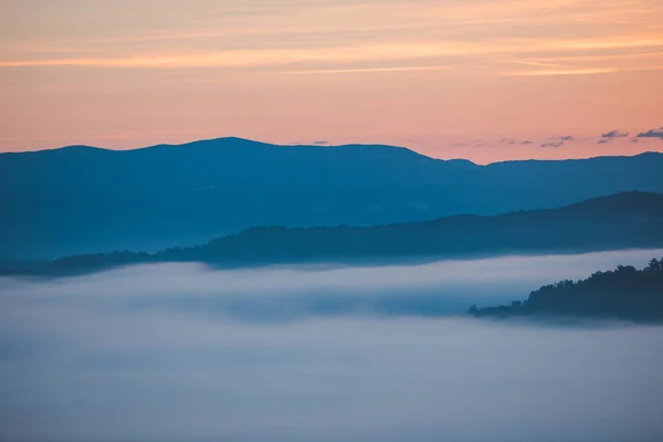 Vista do nascer do sol sobre a névoa das montanhas e nuvens sob picos — Fotografia de Stock