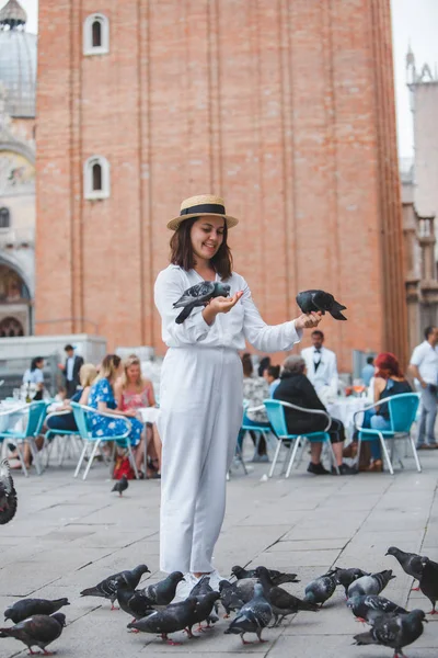 Beyaz giysili, hasır şapkalı kadın Venedik Meydanı 'nda güvercinlerle eğleniyor.