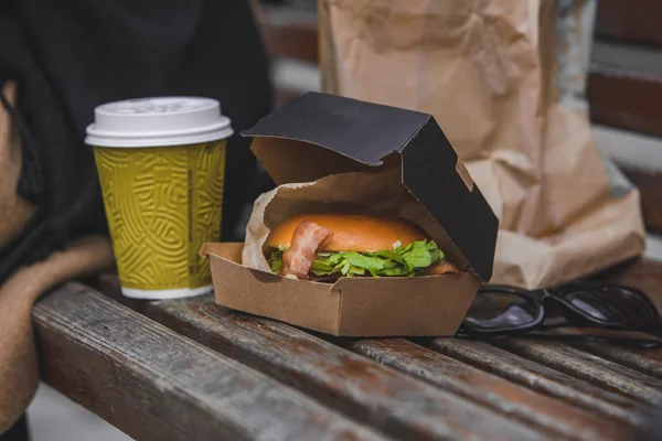 Fastfood. grote hamburger met kopje thee op een bankje. — Stockfoto