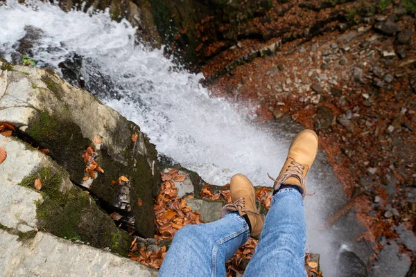 Vrouw in blauwe jeans en bruine laarzen zittend op de rand kijken naar waterval — Stockfoto