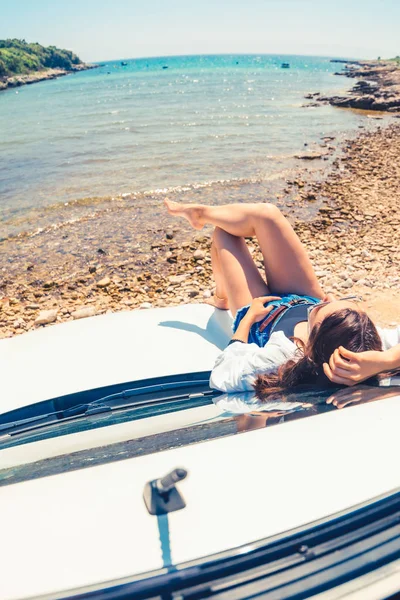 Vrouw het leggen van de auto kap met uitzicht op zee zomer strand — Stockfoto
