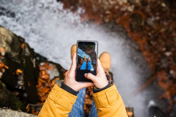 Mujer tomando la foto en el teléfono de sus piernas con cascada en el fondo — Foto de Stock