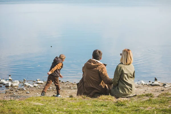 Famiglia a piedi vicino all'acqua. seduto sulla spiaggia. bambino che lancia sassi in acqua — Foto Stock