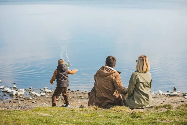 가족이 물 근처를 걷고 있습니다. 해변에 앉아. 물에 바위를 던지는 작은 아이 — 스톡 사진