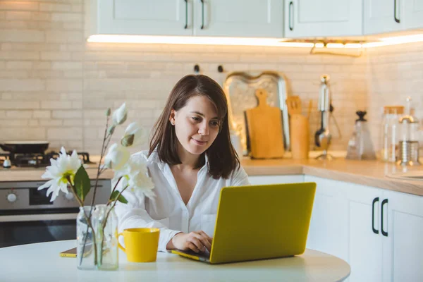 Jovem muito caucasiano mulher falando no telefone sentado na frente de laptop na cozinha — Fotografia de Stock