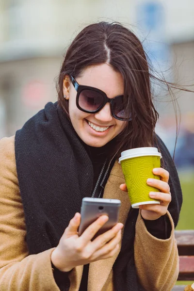 Woman with phone sitting on bench drinking coffee — Stock Photo, Image