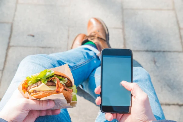 Man holding burger and mobile phone. white screen — Stock Photo, Image