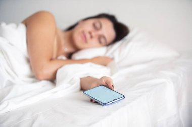 elinde yatakta telefon uyuyan kadın
