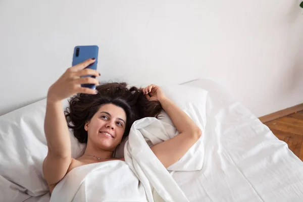 Woman laying in bed taking selfie on the phone — Stock Photo, Image