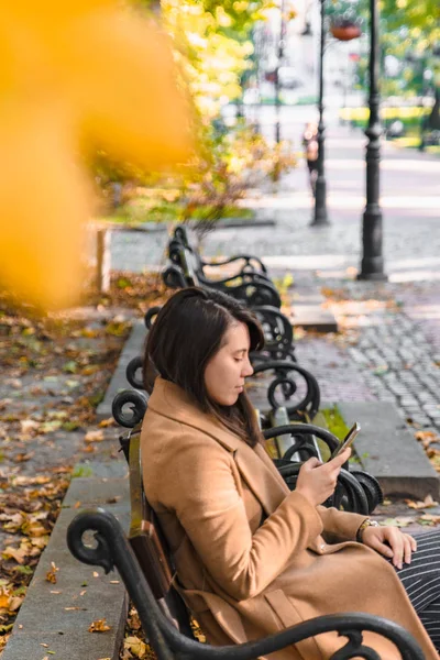 Young adult fashion woman sitting at city park bench in autumn fall season — Stock Photo, Image