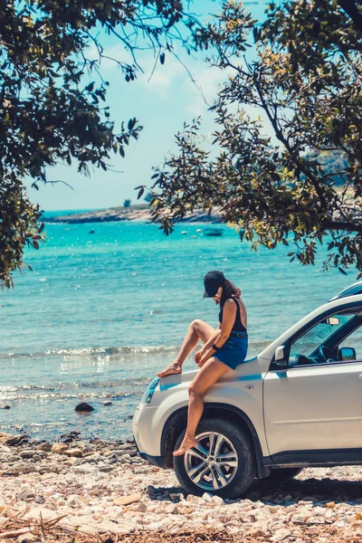 Frau sitzt auf Motorhaube und blickt auf den Strand am Meer — Stockfoto