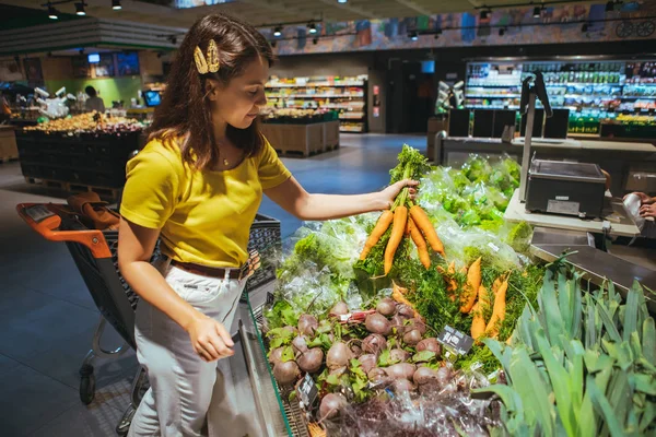 Joven bastante adulto mujer tomando zanahorias de supermercado estante — Foto de Stock