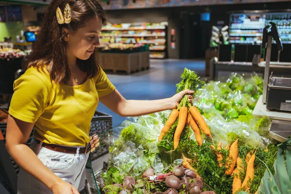 Joven bastante adulto mujer tomando zanahorias de supermercado estante — Foto de Stock