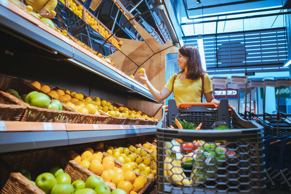 woman taking oranges from supermarket store shelf