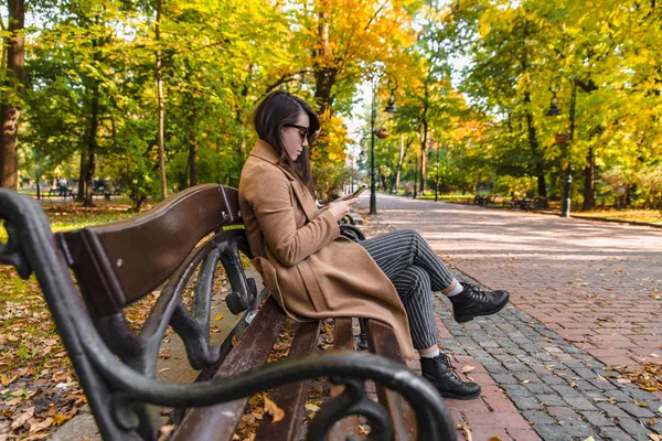 Fiatal felnőtt divat nő ül a városi parkban padon őszi szezon — Stock Fotó