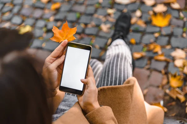 Vrouw houdt telefoon met wit scherm buitenshuis gele esdoorn blad — Stockfoto