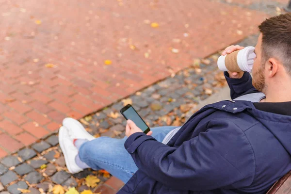 No face man sitting on the bench at city park drinking coffee surfing on phone — Stock Photo, Image