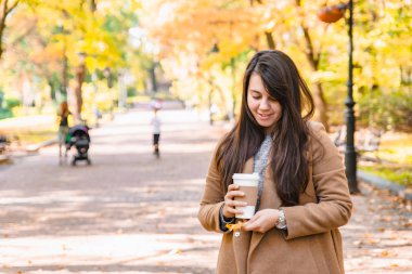 Elinde kahve fincanı tutan kadın sonbahar sezonuna gitmek için içiyor.