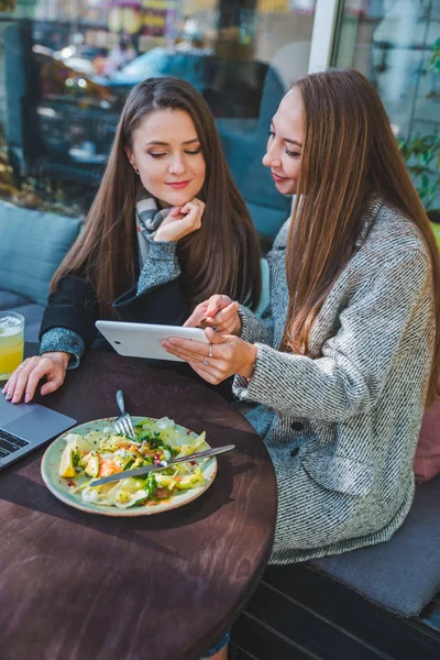 Дві молоді дорослі жінки зустрічаються у відкритому кафе, що працює на ноутбуці — стокове фото