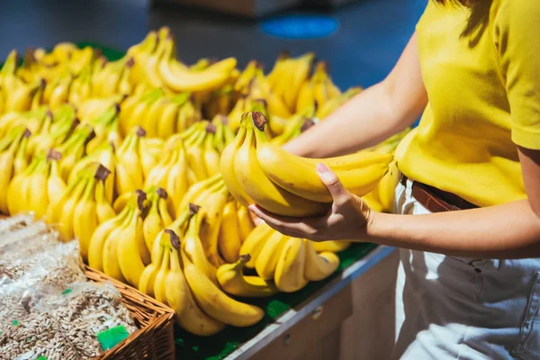 Nainen ottaa keltaisia banaaneja myymälän hyllyltä — kuvapankkivalokuva