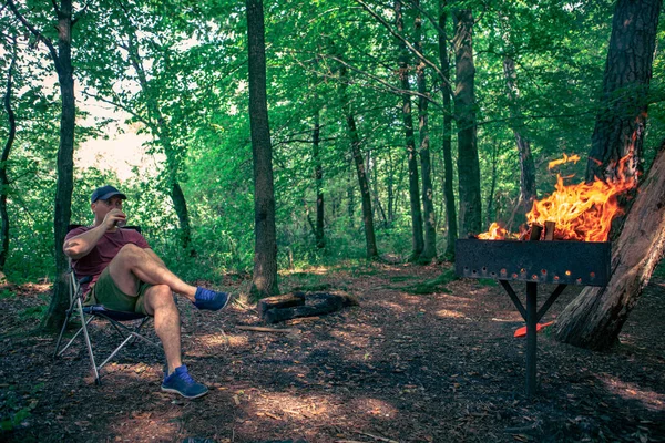 Άνθρωπος κάθεται σε καρέκλα στρατόπεδο πίνοντας μπίρες BBQ φωτιά — Φωτογραφία Αρχείου