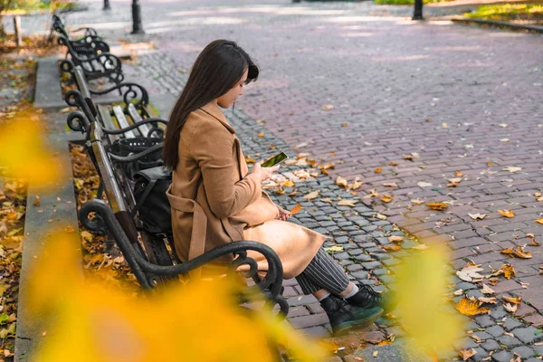 秋の秋のシーズンに都市公園のベンチに座っている若い大人のファッション女性 — ストック写真