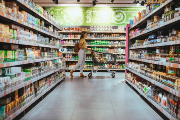 Mulher com compras entre prateleira da loja — Fotografia de Stock