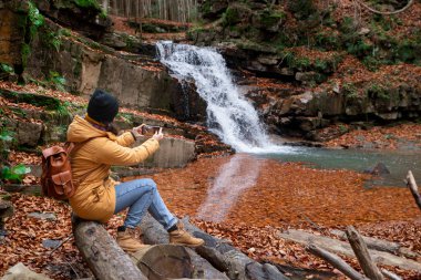şelale sonbahar sezonu bakarak kütük üzerinde oturan kadın