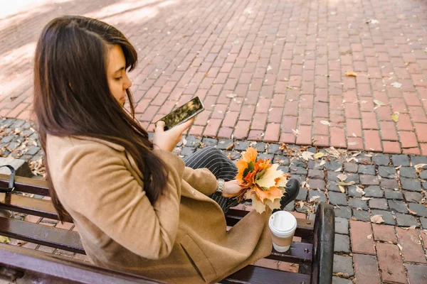 Mujer sentada en el parque de la ciudad tomando café tomando fotos de ramo de hojas de arce —  Fotos de Stock