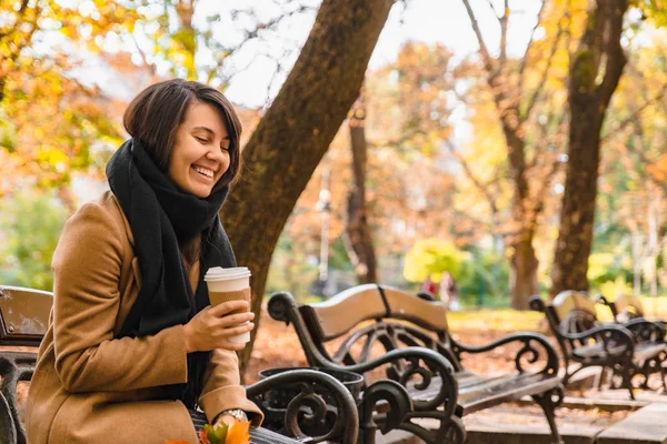 Vrouw zitten op de bank in de herfst stadspark het drinken van koffie — Stockfoto
