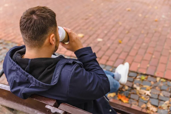 Man sitting on the bench at city park drinking coffee surfing on phone — Stock Photo, Image