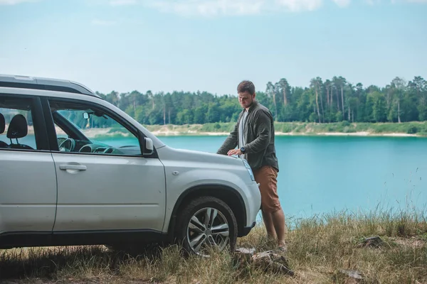 Homem do conceito do curso de carro que olha no homem no lago da capa do carro do SUV no fundo — Fotografia de Stock