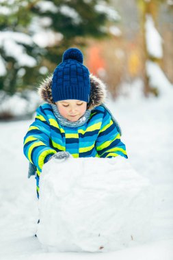 Küçük tatlı çocuk kardan adam yapıyor. yuvarlanan büyük kartopu