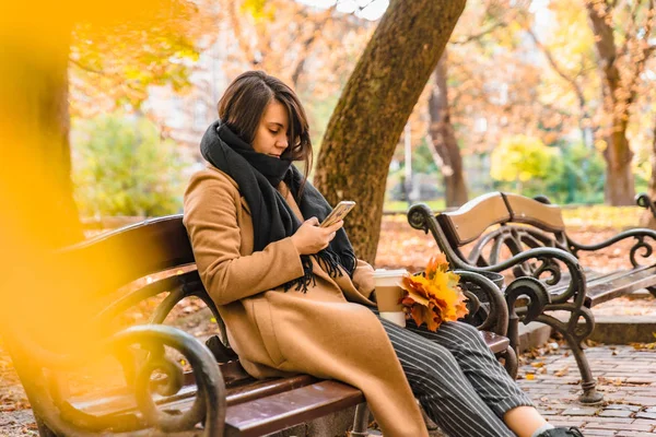 Woman sitting in city park drinking coffee taking picture of bouquet of maple leaves — Stock Photo, Image
