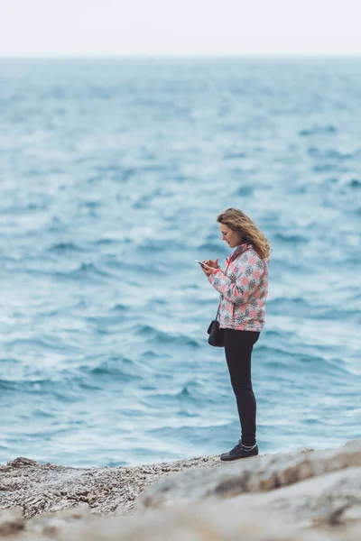 Jeune femme en manteau au bord de la mer regardant la mer orageuse — Photo