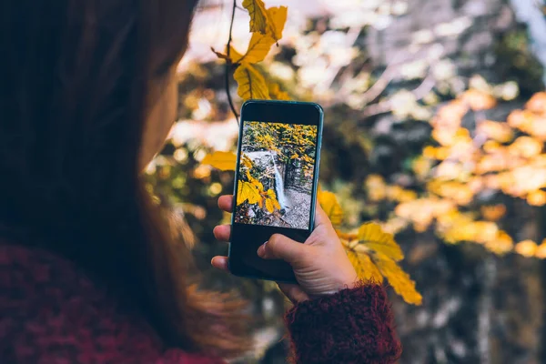 Woman taking picture of autumn waterfall on the phone — Stock Photo, Image