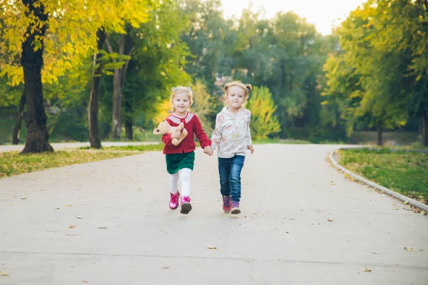 Дві дівчинки-подружки грають в осінньому міському парку, тримаючись за руки — стокове фото