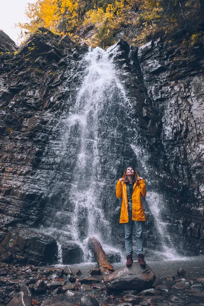 Vrouw in gele regenjas bij herfst waterval — Stockfoto