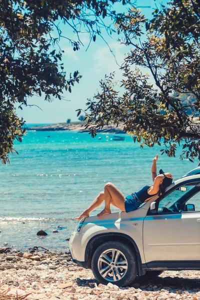 Frau sitzt auf Motorhaube und blickt auf den Strand am Meer — Stockfoto