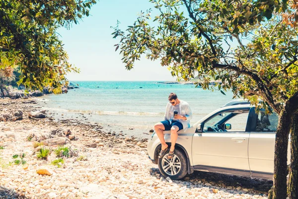 Mann mit Kaffeetasse steht neben Auto am Strand — Stockfoto