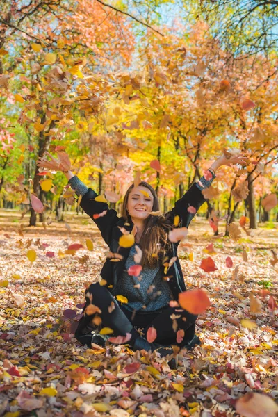 Młoda ładna kobieta bawi się żółtymi jesiennymi liśćmi w parku miejskim — Zdjęcie stockowe