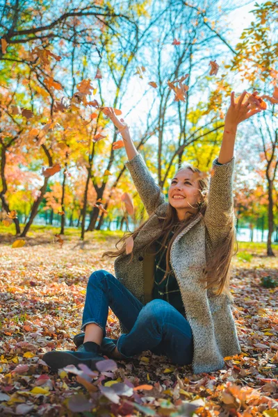 Молода красива жінка грає з жовтим осіннім листям у міському парку — стокове фото