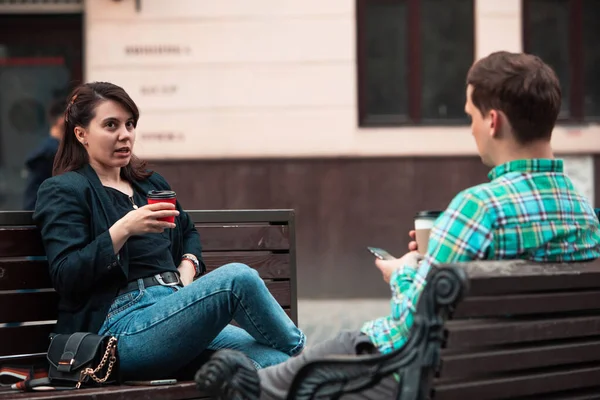 Pasangan yang tersenyum duduk di bangku berbicara satu sama lain minum kopi — Stok Foto