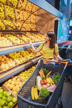 süpermarket mağaza rafından portakal alan kadın